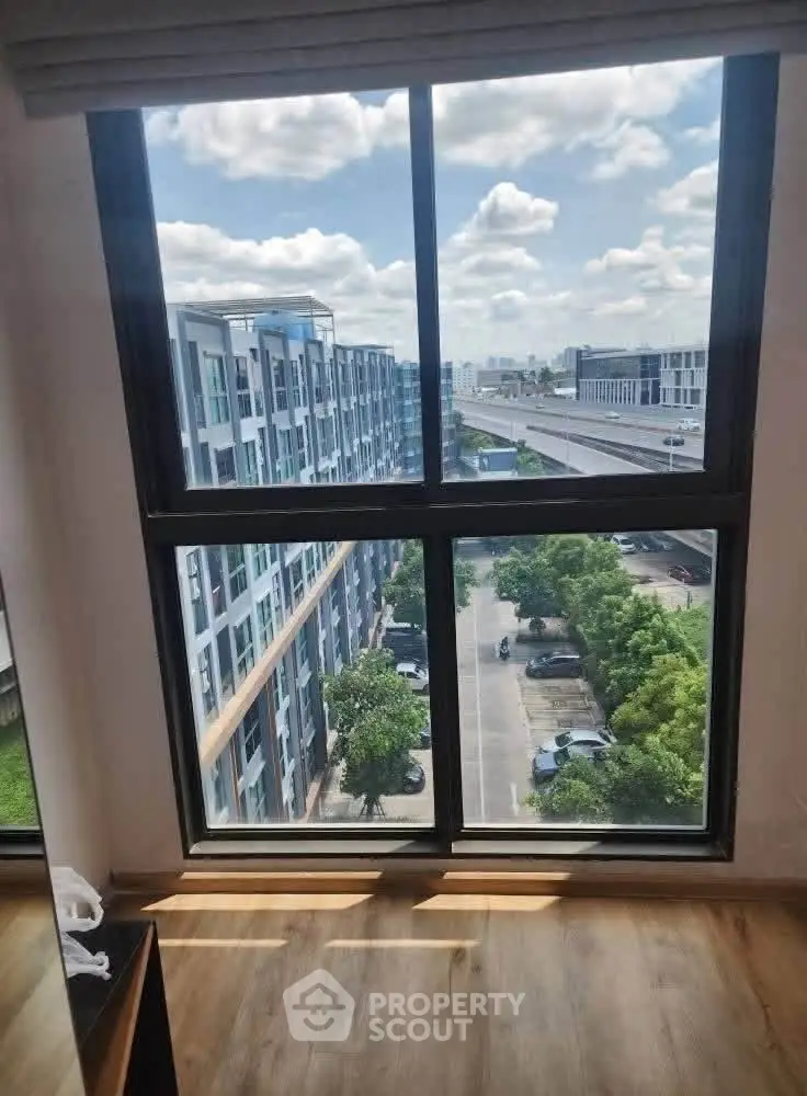 Stunning high-rise view from modern apartment window overlooking cityscape and lush greenery.