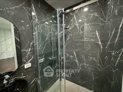 Luxurious modern bathroom with sleek black marble tiles and glass shower enclosure.