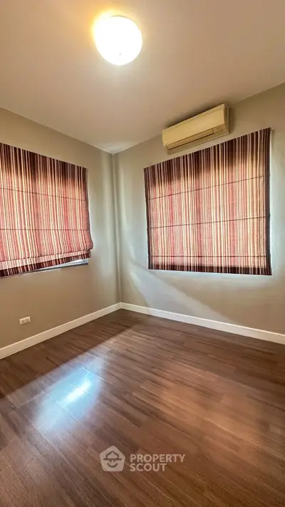 Spacious empty room with wooden flooring and striped curtains, perfect for customization.