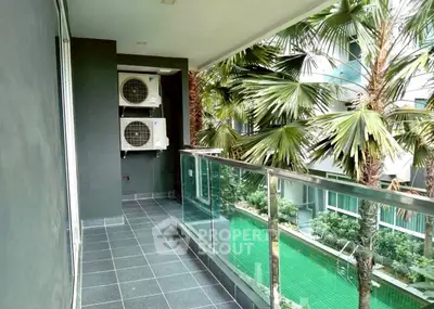 Modern balcony with glass railing overlooking lush garden and pool area.