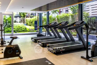 Modern gym with treadmills and exercise equipment overlooking lush garden view.