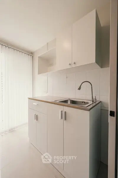 Modern compact kitchen with sleek white cabinetry and stainless steel sink, perfect for urban living.