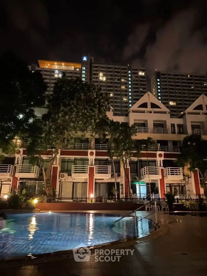 Stunning night view of a residential building with illuminated pool and lush greenery.
