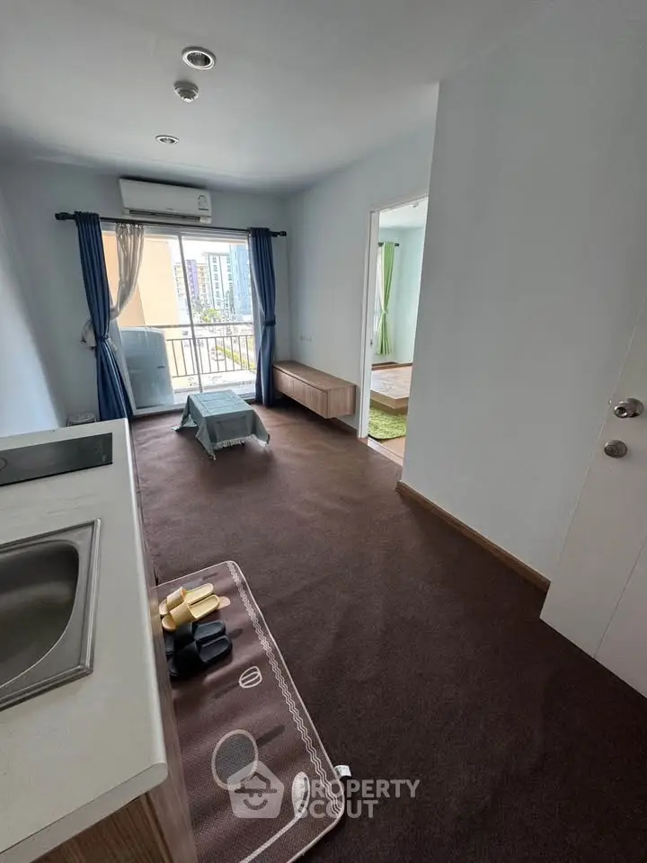 Modern apartment interior with compact kitchen and cozy living area, featuring a small balcony with city views.