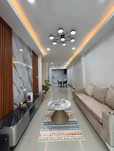 Modern living room with stylish decor and open layout leading to dining area, featuring elegant lighting and marble accents.