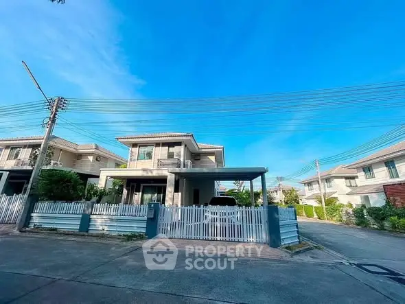 Charming suburban house with white picket fence and spacious driveway under clear blue sky.