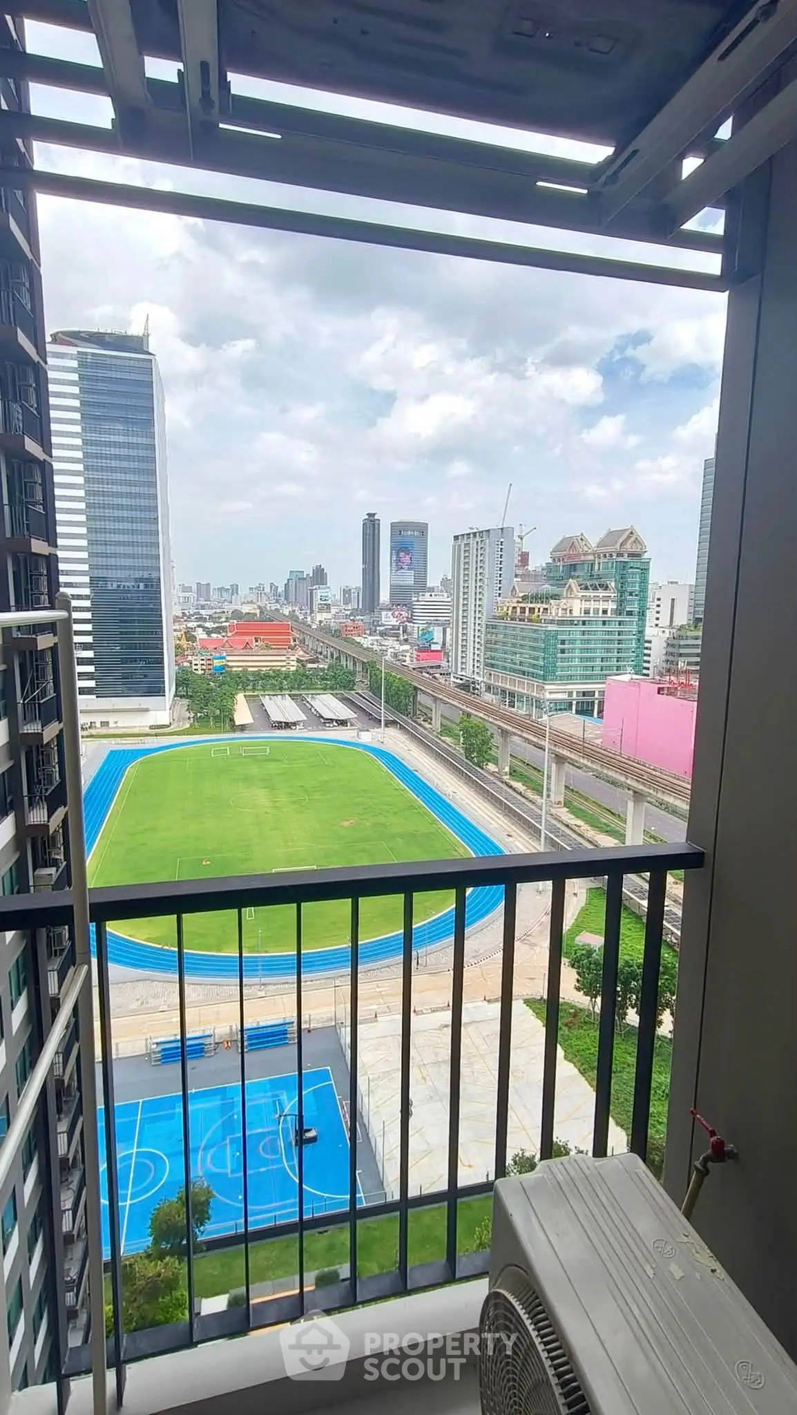 Stunning cityscape view from a high-rise balcony overlooking sports fields and urban skyline.
