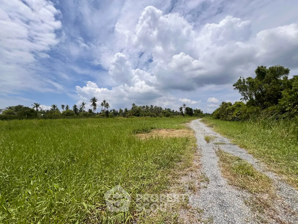 Expansive green field with a gravel path under a cloudy sky, ideal for development.