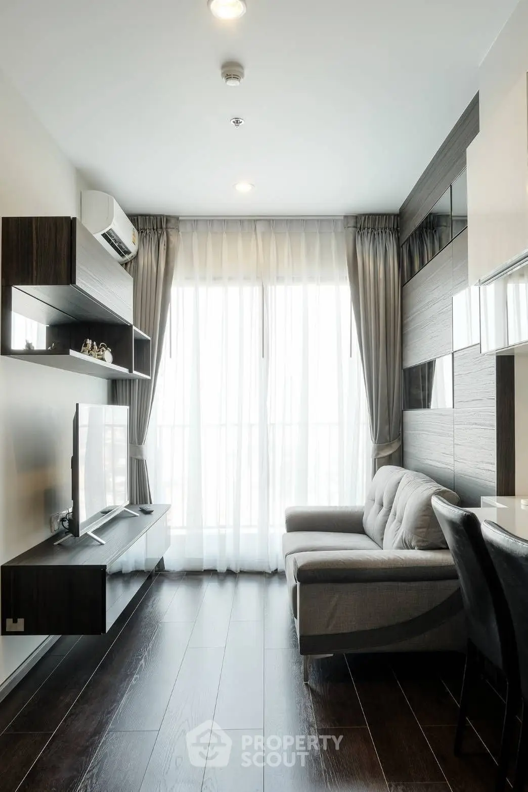 Modern living room with sleek furniture and large window, featuring elegant wood flooring and stylish decor.