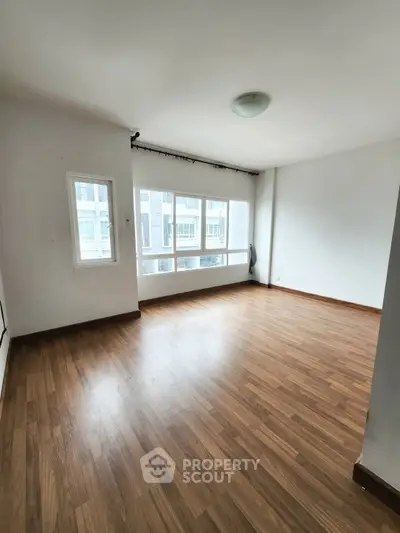 Spacious empty room with large windows and wooden flooring, ideal for customization.