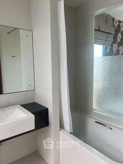 Modern bathroom with sleek sink and bathtub, featuring frosted glass window for privacy.
