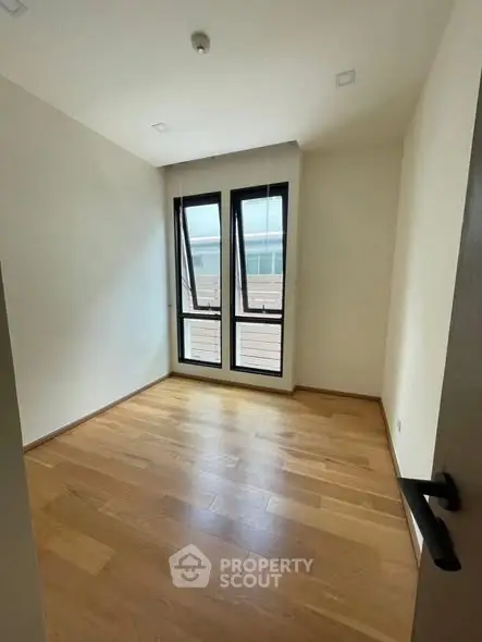 Spacious empty room with wooden flooring and large windows, perfect for customization.