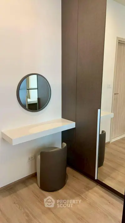 Modern bedroom with stylish vanity and mirror, featuring sleek wood flooring and contemporary design.