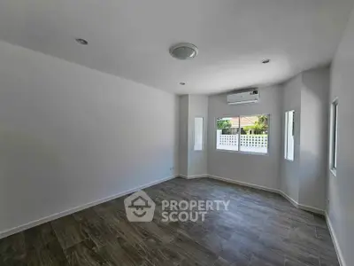 Spacious empty room with wooden flooring and large windows offering natural light.