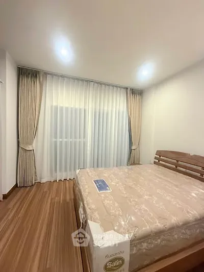 Spacious bedroom with elegant wooden flooring and large window with curtains, perfect for relaxation.