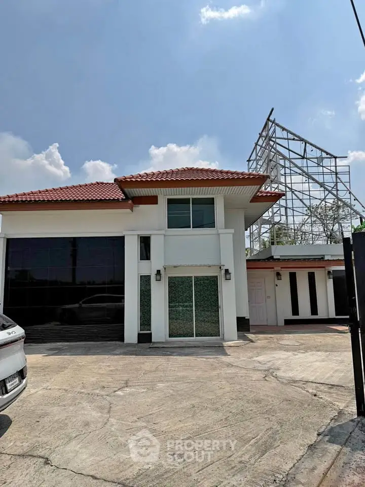 Charming two-story house with red-tiled roof and spacious driveway under a clear blue sky.