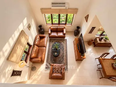Spacious living room with leather sofas and large windows offering lush garden views.