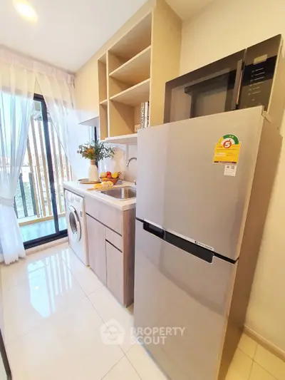 Modern kitchen with fridge, washing machine, and open shelving in bright apartment