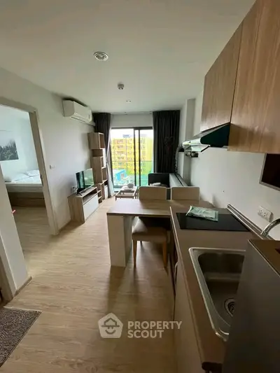 Modern apartment interior with open kitchen and living area, featuring wooden flooring and large windows.