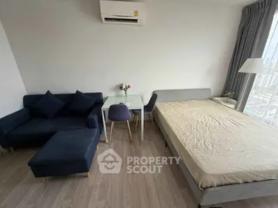 Modern studio apartment with cozy bed, stylish sofa, and dining area, offering a bright and inviting living space.