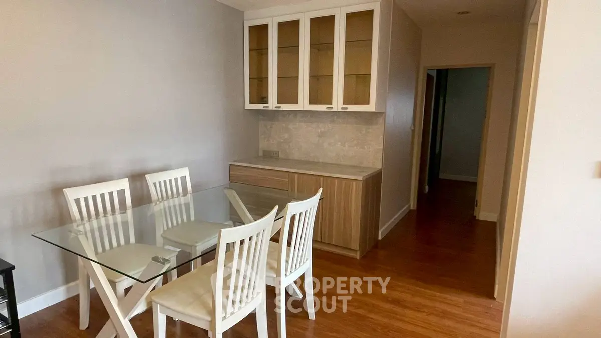Modern dining area with glass table and white chairs, featuring built-in wooden cabinets.