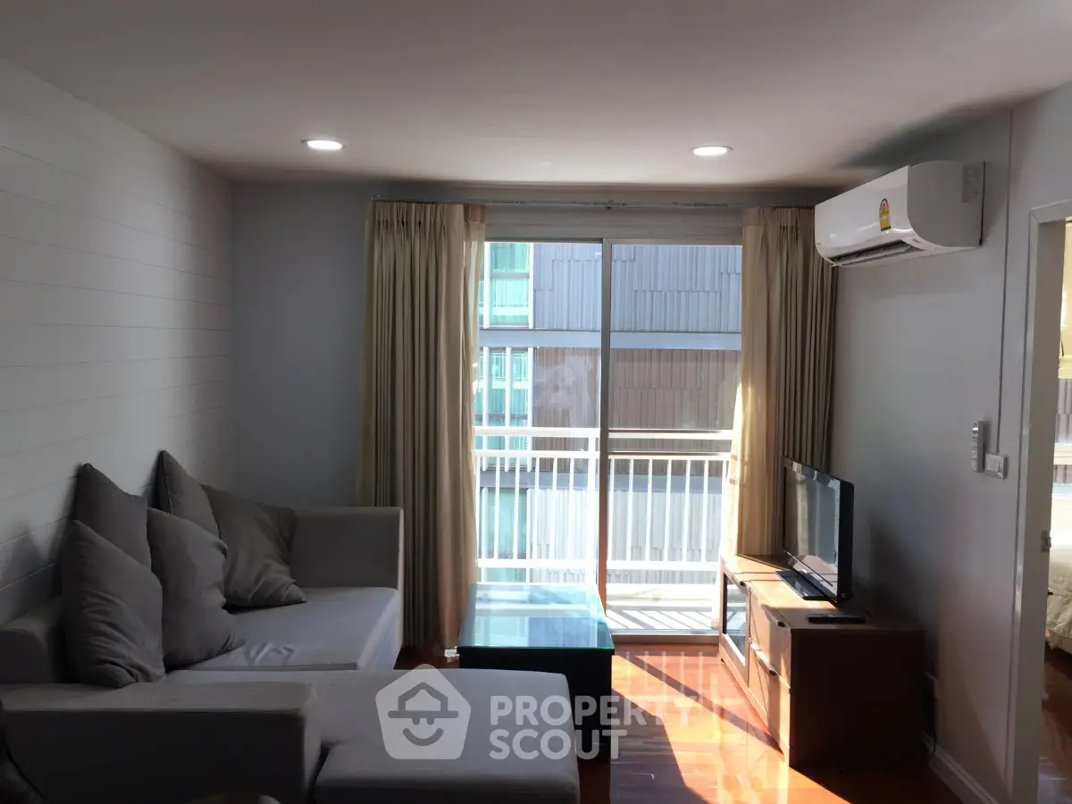 Modern living room with cozy gray sofa, air conditioning, and natural light from large window.