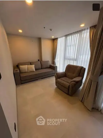 Spacious living room with modern sofa and armchair, large windows with elegant curtains.