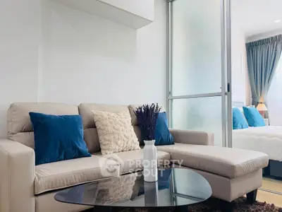 Modern living room with stylish beige sofa and blue cushions, adjacent to a cozy bedroom with elegant decor.