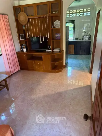 Charming living room with built-in wooden entertainment center and view into cozy kitchen.