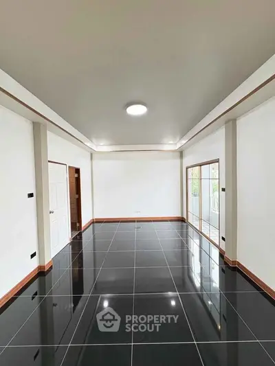 Spacious modern living room with glossy black tile flooring and large windows for natural light.