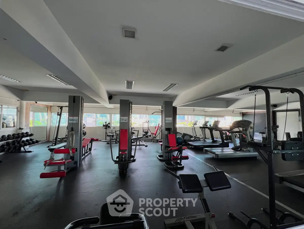 Spacious gym with modern fitness equipment and large windows for natural light.