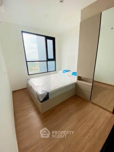 Modern bedroom with large window and wooden flooring in a high-rise apartment.