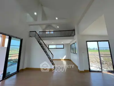 Spacious modern living room with high ceilings and mezzanine, featuring large windows and natural light.
