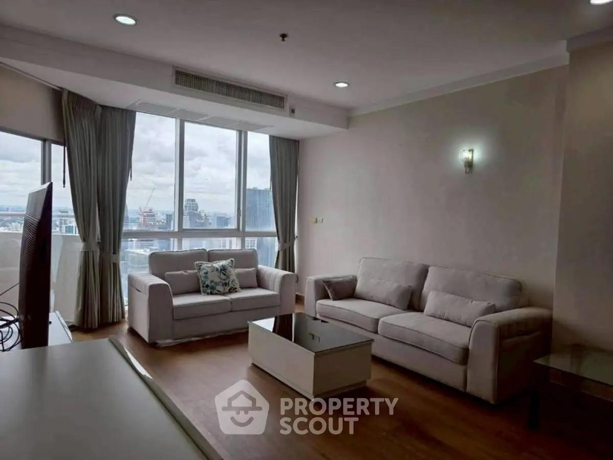 Spacious living room with large windows and city view, featuring modern sofas and a coffee table.