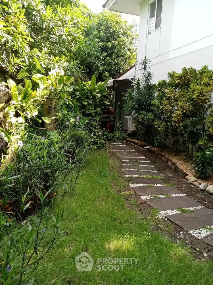 Charming garden pathway beside a modern home with lush greenery and stepping stones.