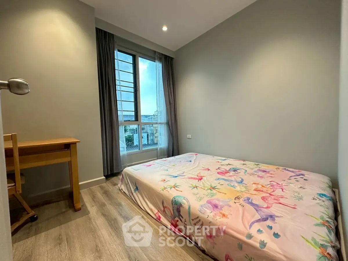 Cozy bedroom with large window and wooden flooring, featuring a charming bedspread.