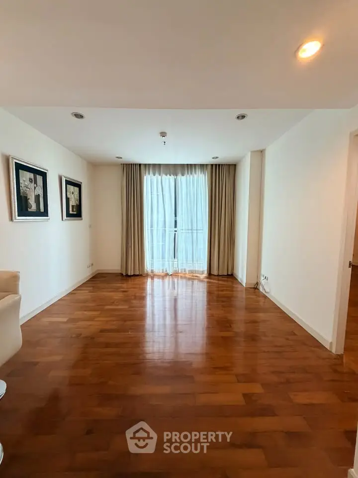 Spacious living room with wooden flooring and large window with curtains, perfect for natural light.