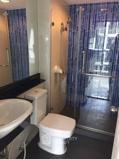 Modern bathroom with sleek design, featuring a glass shower enclosure and stylish blue tile accents.