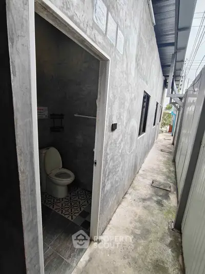 Narrow exterior alley with a small bathroom entrance in a concrete building.