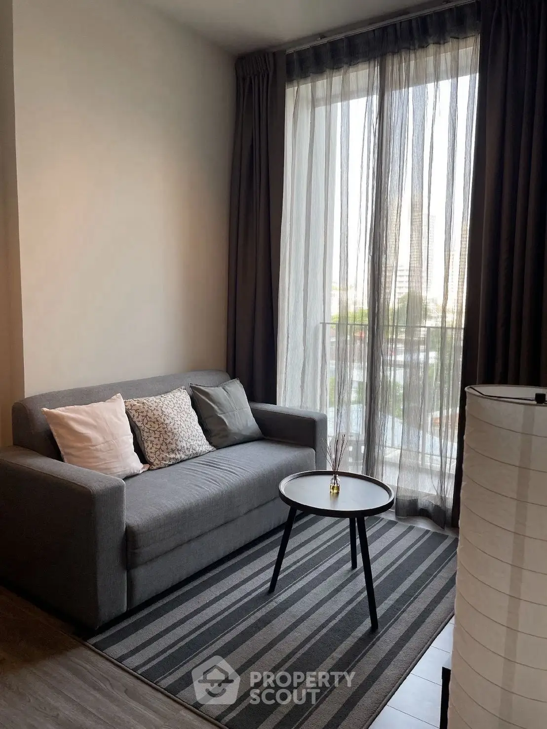 Cozy living room with modern sofa and floor-to-ceiling window offering city view.