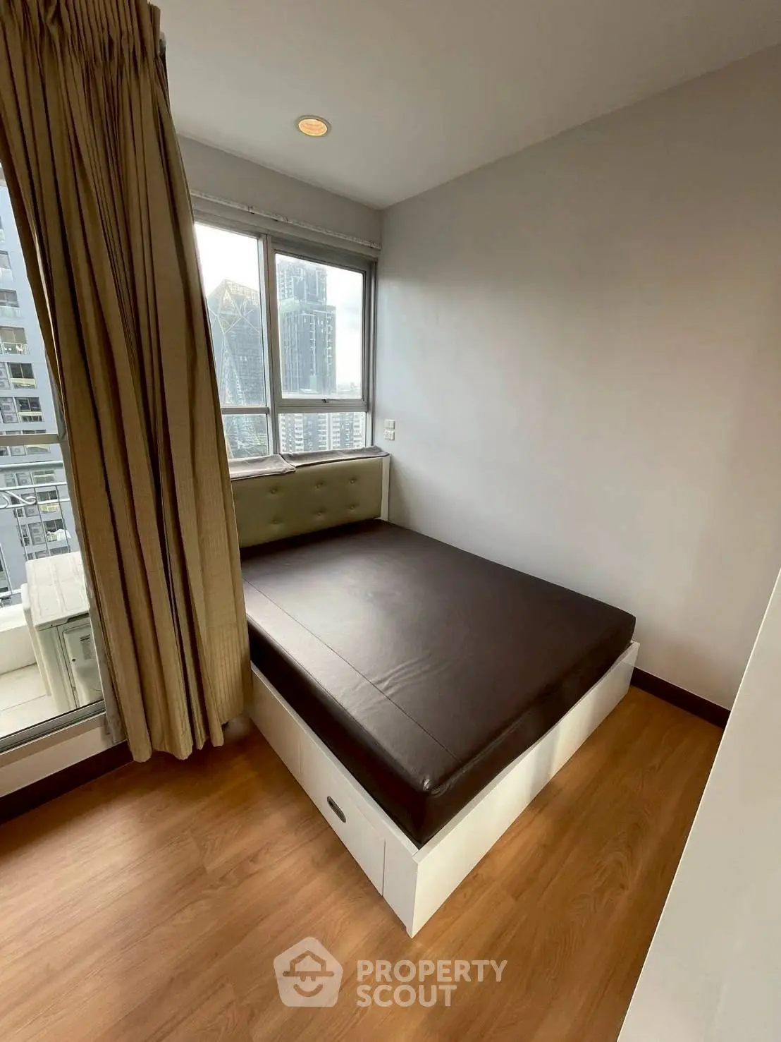 Cozy bedroom with city view, featuring a comfortable bed and large windows for natural light.