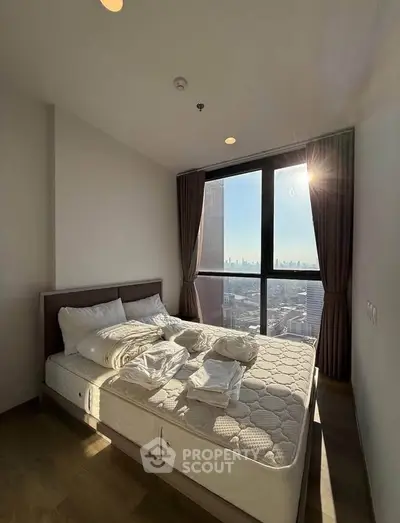 Bright bedroom with city view, featuring a cozy bed and large window letting in natural light.