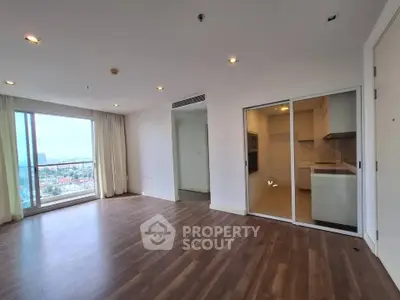 Spacious modern living room with large windows and separate kitchen area in a high-rise apartment.