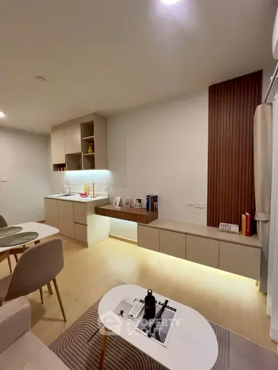 Modern living room with sleek furniture and integrated kitchen area, featuring ambient lighting and stylish decor.