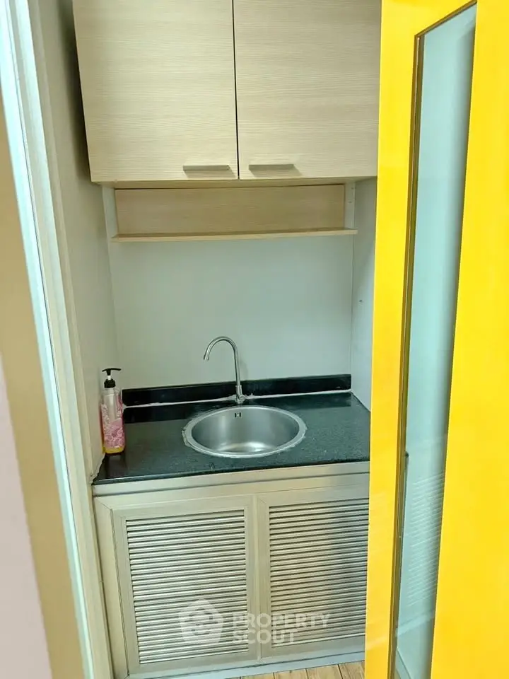 Compact kitchen area with modern sink and yellow door, ideal for small apartments.