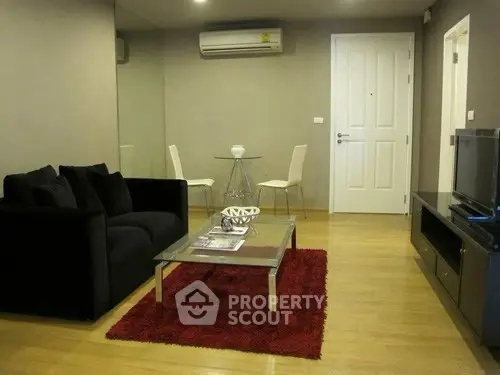 Modern living room with sleek furniture and wooden flooring, featuring a cozy black sofa and stylish decor.