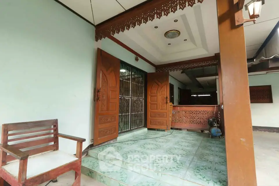 Charming entrance with wooden doors and decorative ceiling in a serene residential setting.