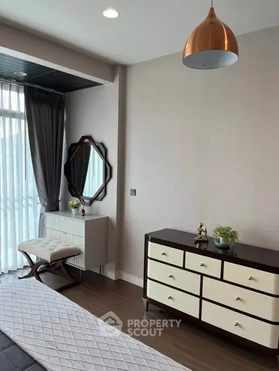 Stylish bedroom with modern furniture and elegant decor, featuring a chic dresser and a cozy seating area.