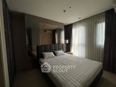 Luxurious bedroom with a large bed, elegant dark furnishings, and ample natural light filtering through sheer curtains.