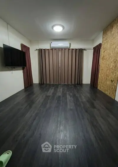 Spacious living room with dark wood flooring and wall-mounted TV, perfect for modern living.